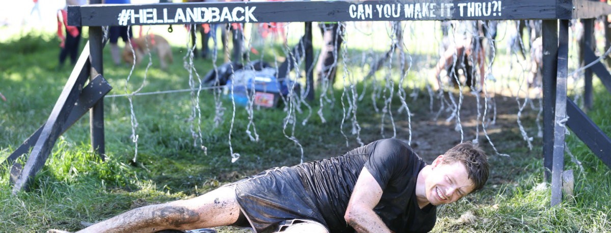 A man is lying down on the ground during the Focus Ireland's Hell and Back event. He is covered in mud.