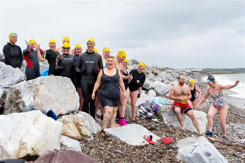 A group of take the plunge participants stand on a beach