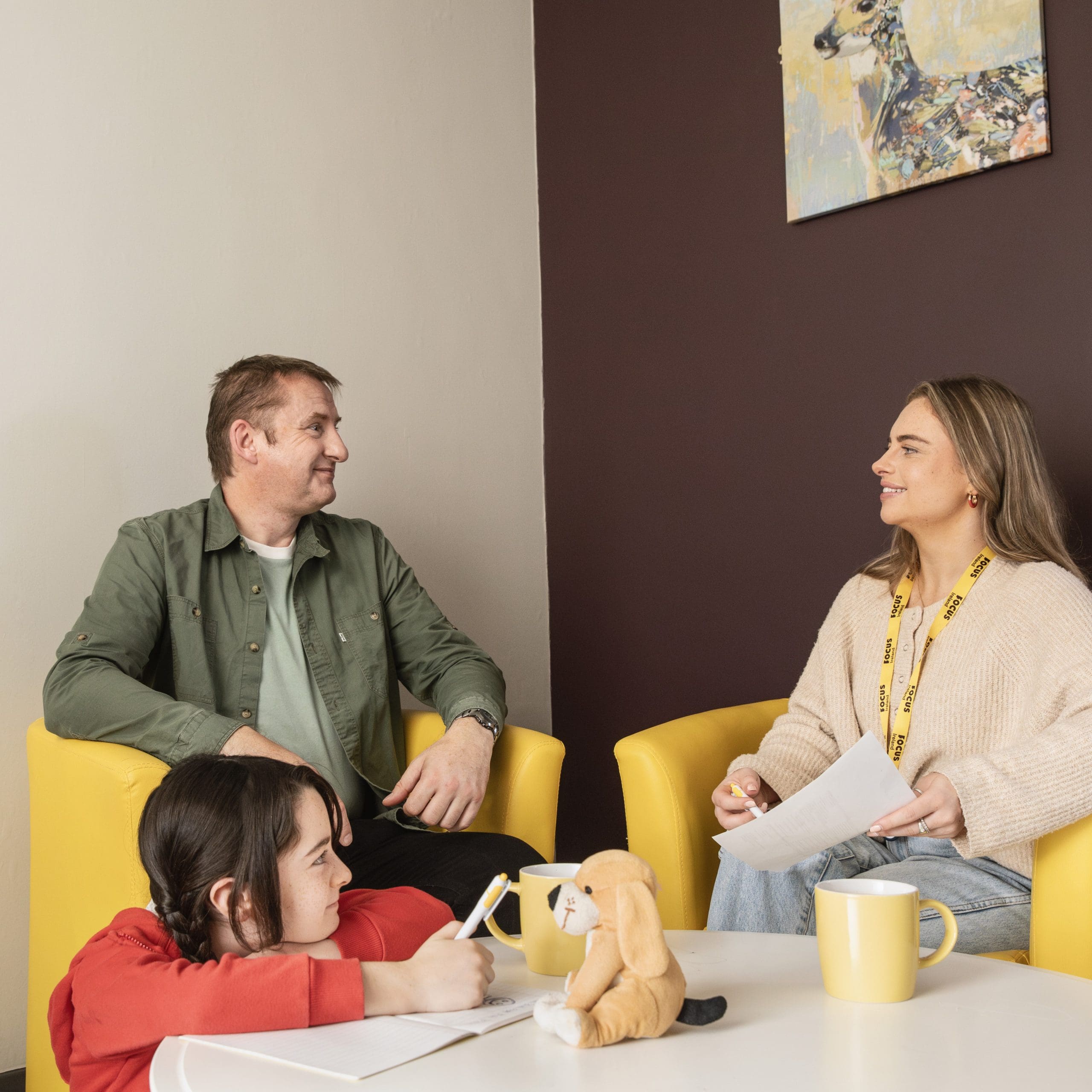 A Focus Ireland employee speaks to a man as their daughter draws on a piece of paper in the foreground. The man is smiling.