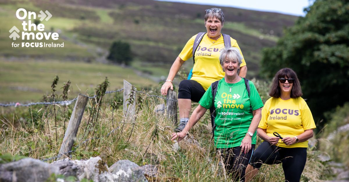 Three hikers smile to camera as they take on Croagh Patrick. Two of them are wearing yellow Focus Ireland t-shirts while the other wears a green on the move t-shirt