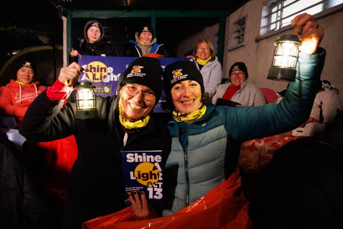 Two people hold up lanterns while sleeping out for Focus Ireland