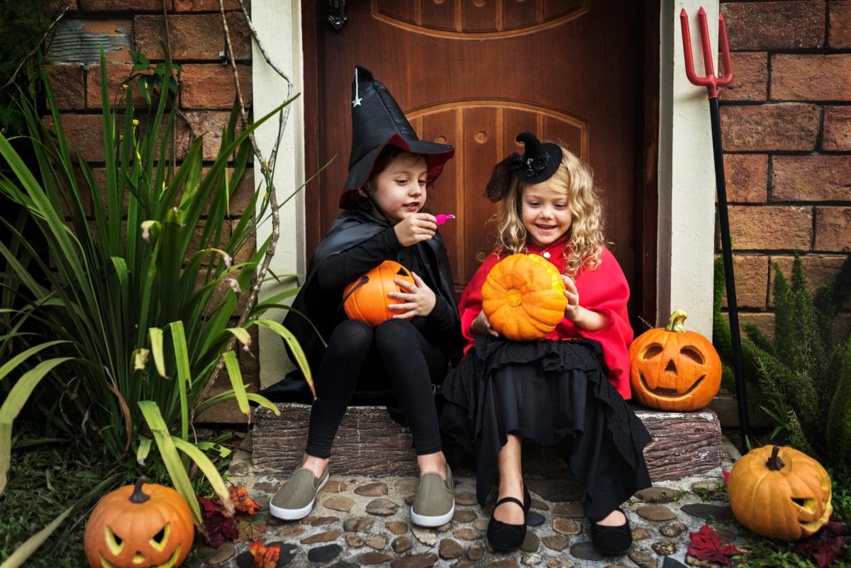 Two children dressed in Halloween costumes. They are both holding pumpkins.