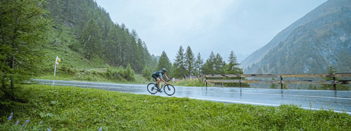 A cyclist rides their bike. They are cycling past a lake in the mountains